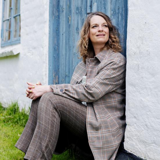 Charlotte Weitze siddende ved dør til landejendom