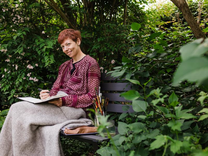 Camilla Brix i gang med at male på bænk i have