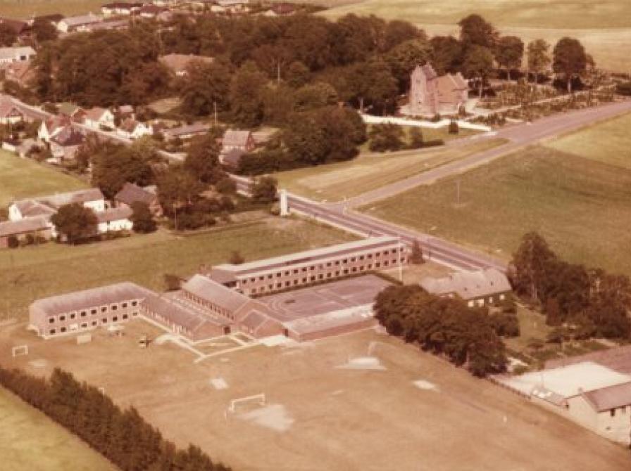 tenmagle Skole ved Sorøvej set fra syd. Den røde bygning til højre er skolebygningen fra 1923.  Forsamlingshuset fra 1937 ses syd for skolen nederst til højre i billedet. Stenmagle Kirke fra 1100-tallet ses for oven.  Klik på billedet for at se det i større udgave!