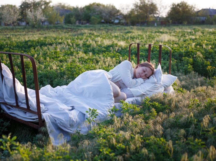 Fotografi af person der sover i seng midt i en mark