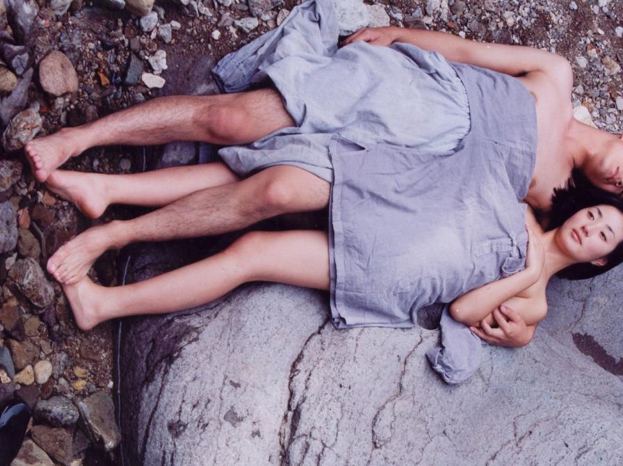 Mand og kvinde ligger på stranden ved siden af hinanden under et tæppe.